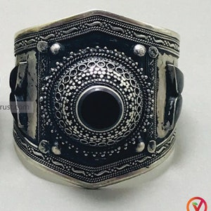 Può includere: Un paio di braccialetti d'argento con disegni intricati e pietre preziose nere. I braccialetti sono larghi e hanno una forma arrotondata.