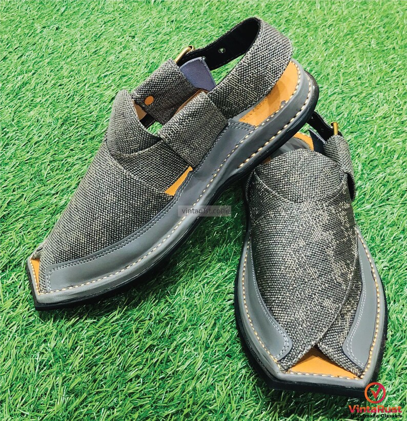 May include: A pair of gray canvas sandals with a pointed toe and a strap across the top of the foot. The sandals have a black leather sole and a brown leather insole.