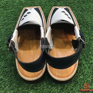 May include: A pair of white leather sandals with black accents and a brown leather insole. The sandals have a strap with a buckle and the number "804" is written on the top of each sandal.