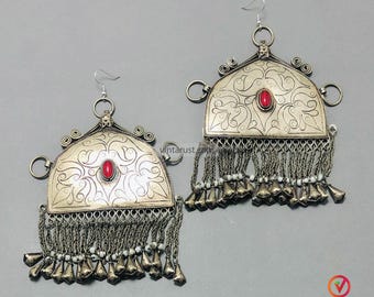 May include: Pair of silver-toned earrings with a red stone center and intricate floral patterns. The earrings have dangling chains with small bells and white beads, and are designed with a hook closure.