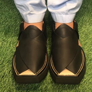 May include: A pair of black leather sandals with a pointed toe and a thick sole. The sandals have a decorative stitch detail around the edges and a small opening at the top of the foot.