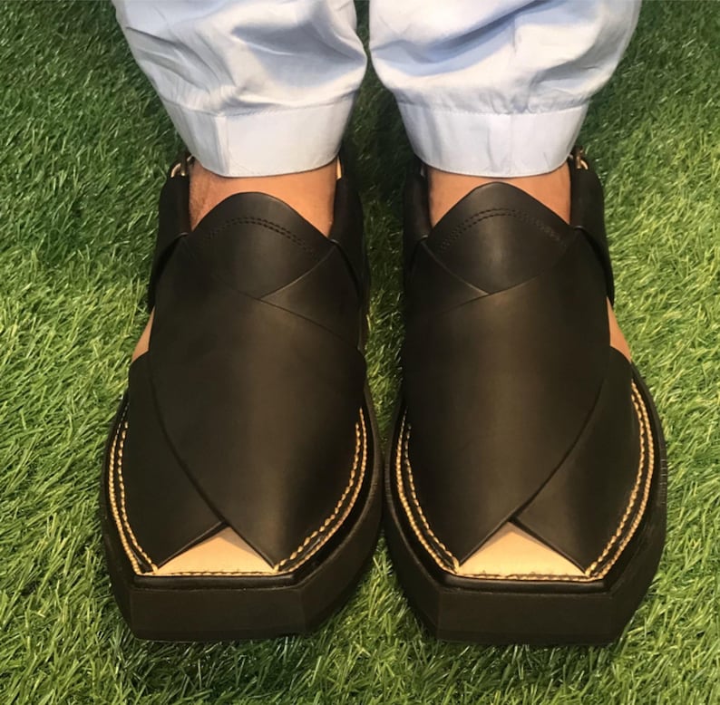 May include: A pair of black leather sandals with a pointed toe and a thick sole. The sandals have a decorative stitch detail around the edges and a small opening at the top of the foot.