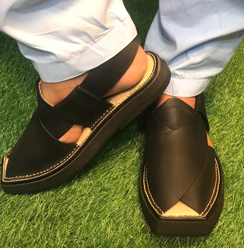 May include: A pair of black leather sandals with a closed toe and a strap around the ankle. The sandals have a thick black sole and are stitched with a yellow thread.