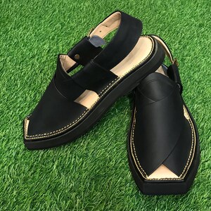 May include: A pair of black leather sandals with a closed toe and an open heel. The sandals have a thick black sole and gold stitching around the edges.