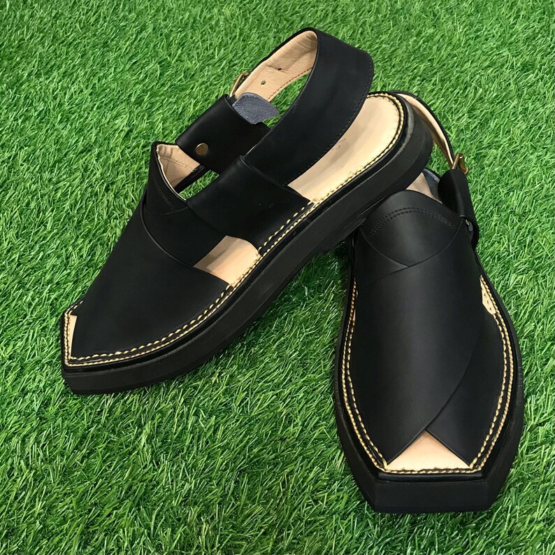 May include: A pair of black leather sandals with a closed toe and an open heel. The sandals have a thick black sole and gold stitching around the edges.