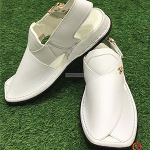 May include: White leather sandals with a buckle closure and a gold accent. The sandals have a pointed toe and a flat sole.