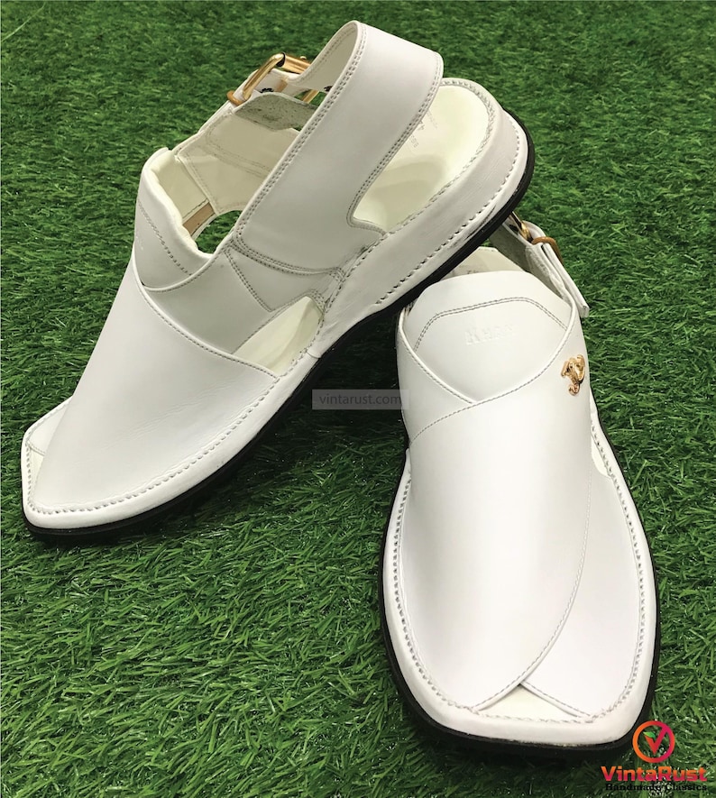 May include: White leather sandals with a buckle closure and a gold accent. The sandals have a pointed toe and a flat sole.
