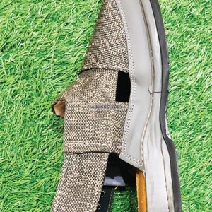 May include: A pair of gray and brown sandals with a woven fabric upper and a rubber sole. The sandals have a cut-out design on the upper and a strap that goes around the ankle.