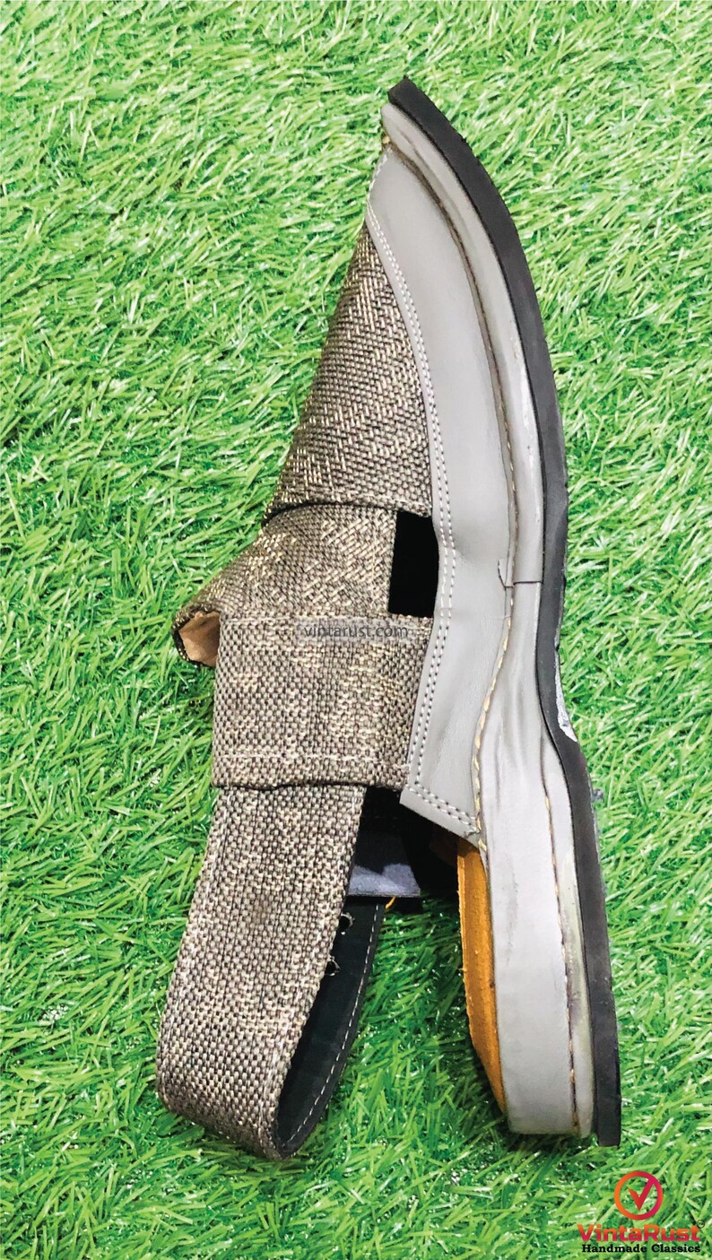 May include: A pair of gray and brown sandals with a woven fabric upper and a rubber sole. The sandals have a cut-out design on the upper and a strap that goes around the ankle.