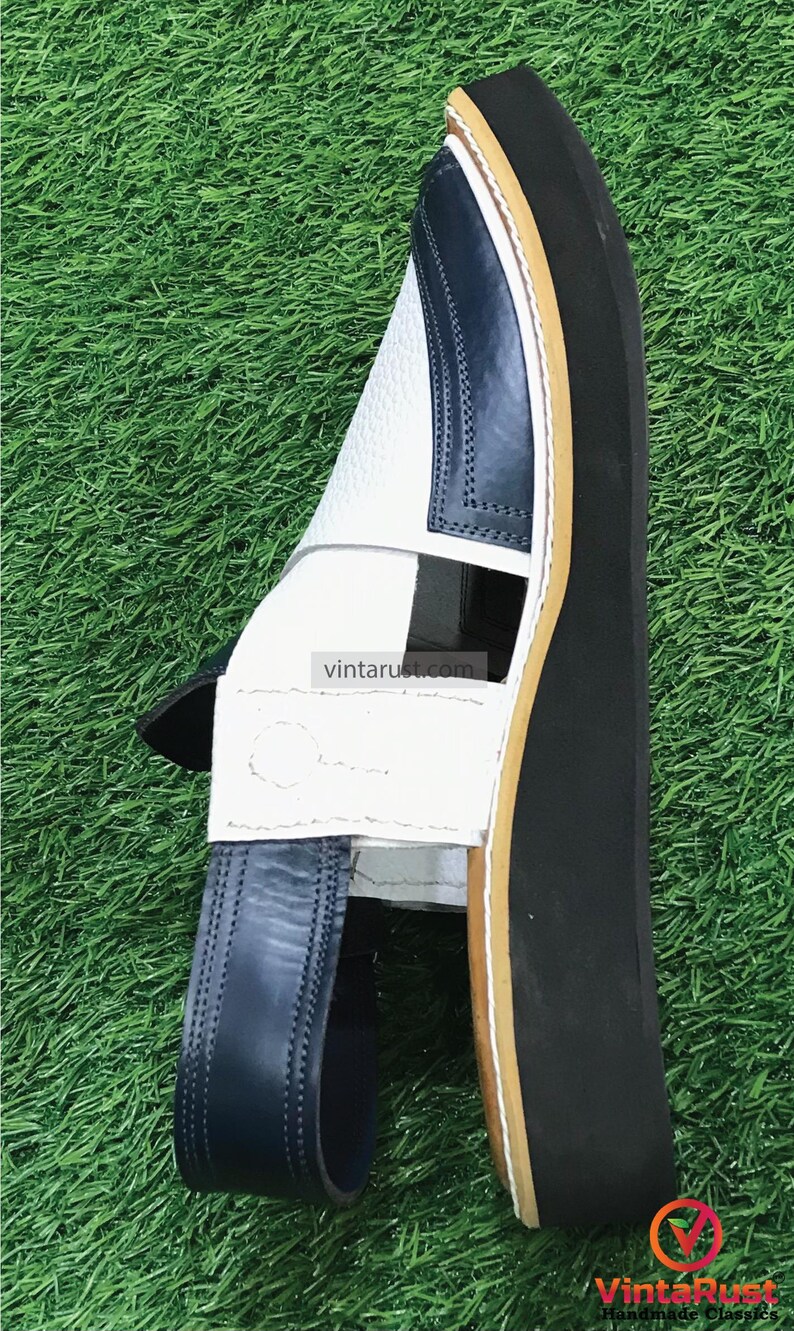 May include: White leather sandals with a blue leather strap and a black rubber sole. The sandals have a unique design with a cut-out detail on the top.
