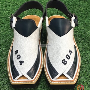 May include: A pair of white and black leather sandals with a strap across the top. The sandals have a brown trim and the number "804" is printed on each sandal.