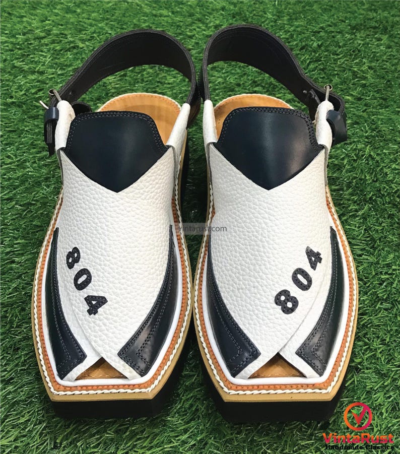 May include: A pair of white and black leather sandals with a strap across the top. The sandals have a brown trim and the number "804" is printed on each sandal.