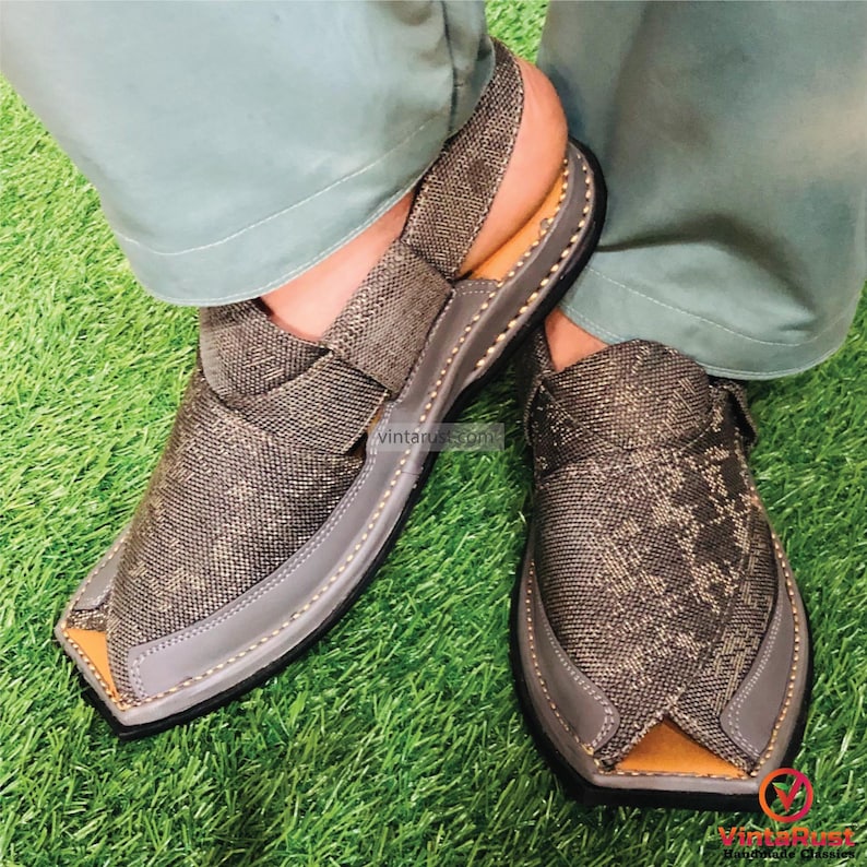 May include: A pair of gray sandals with a patterned fabric upper and a brown leather sole. The sandals have a strap across the top of the foot and an open toe.