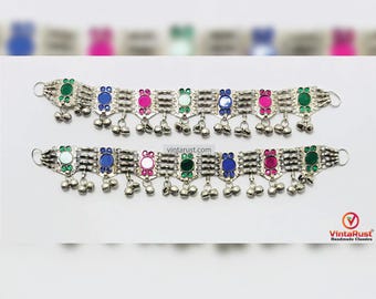 May include: Two silver anklets with bells and colorful glass accents. The anklets have a silver chain with small round green, blue, and pink glass accents. Each anklet has a row of silver bells hanging from the bottom.