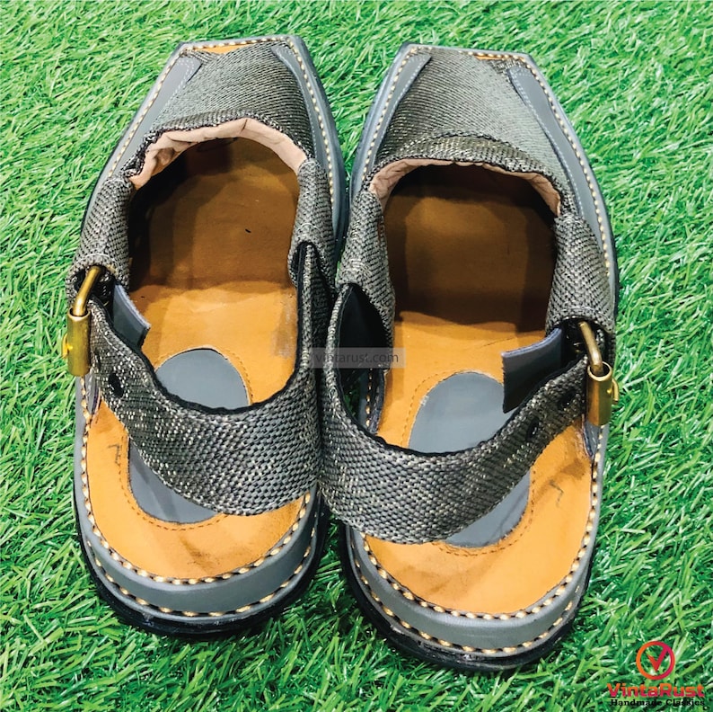 May include: A pair of gray leather sandals with a strap and buckle. The sandals have a brown leather lining and a black rubber sole.