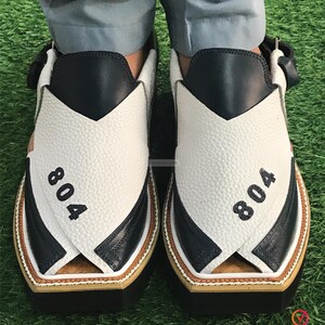 May include: A pair of white and black leather sandals with a criss-cross strap design. The sandals have a brown trim and the number "804" is printed on each sandal.