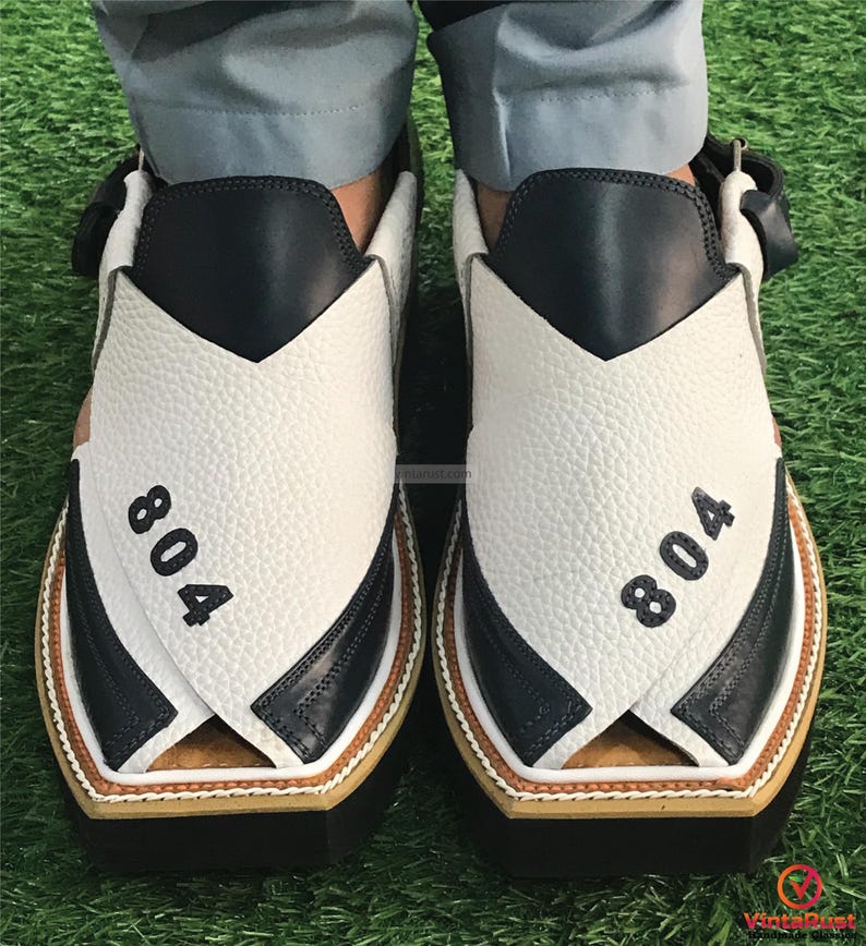 May include: A pair of white and black leather sandals with a criss-cross strap design. The sandals have a brown trim and the number "804" is printed on each sandal.