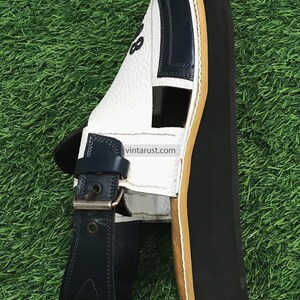 May include: White leather sandals with a blue strap and buckle. The sandals have a thick black sole with a brown edge.