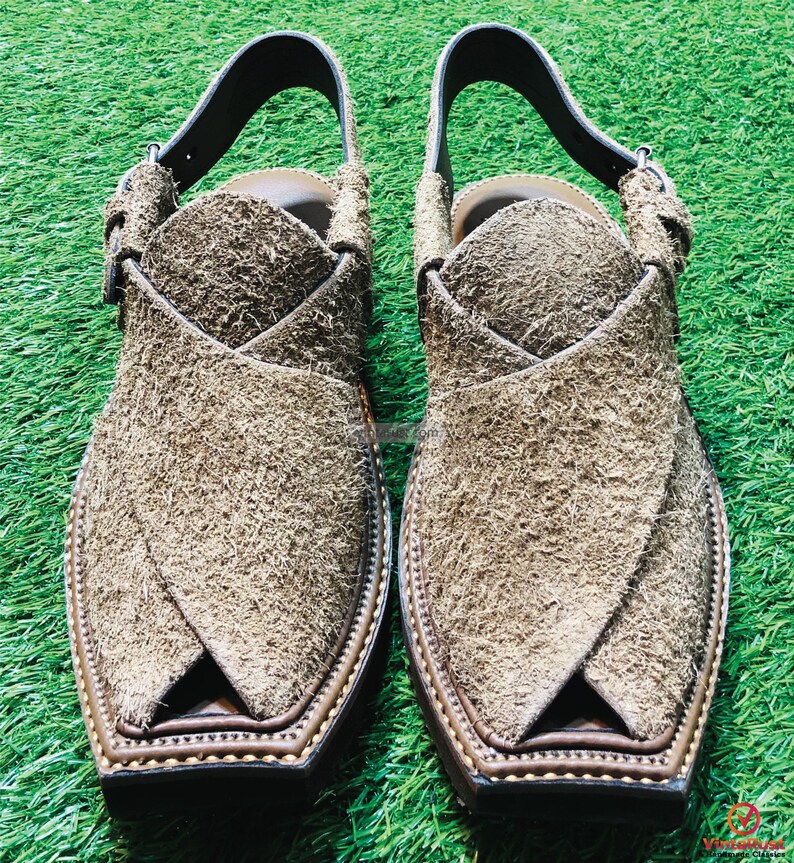May include: A pair of brown suede sandals with a pointed toe and a strap across the top of the foot. The sandals have a brown leather sole and decorative stitching around the edge.
