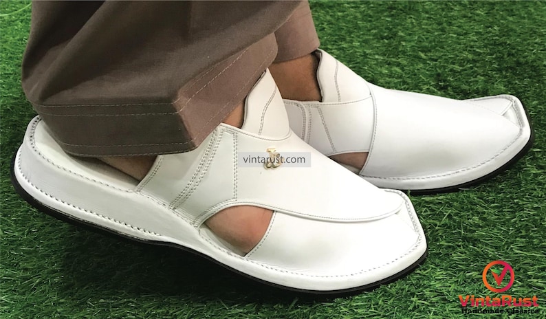 May include: White leather sandals with a closed toe and an open heel. The sandals have a thick white sole and a decorative gold buckle.