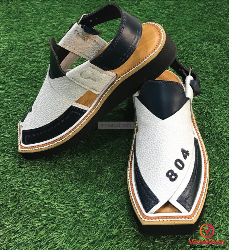 May include: White and navy blue leather sandals with a brown sole. The sandals have a strap across the top and a buckle closure. The sandals have the number "804" printed on the side.