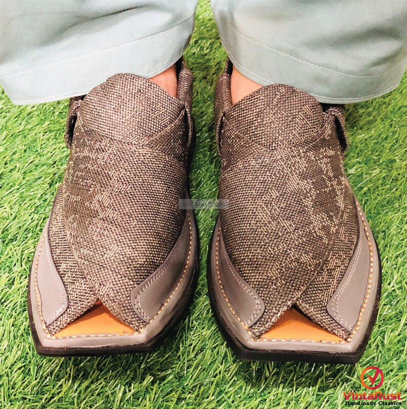 May include: A pair of gray fabric shoes with a pointed toe and a strap across the top. The shoes are worn on a green grassy surface.