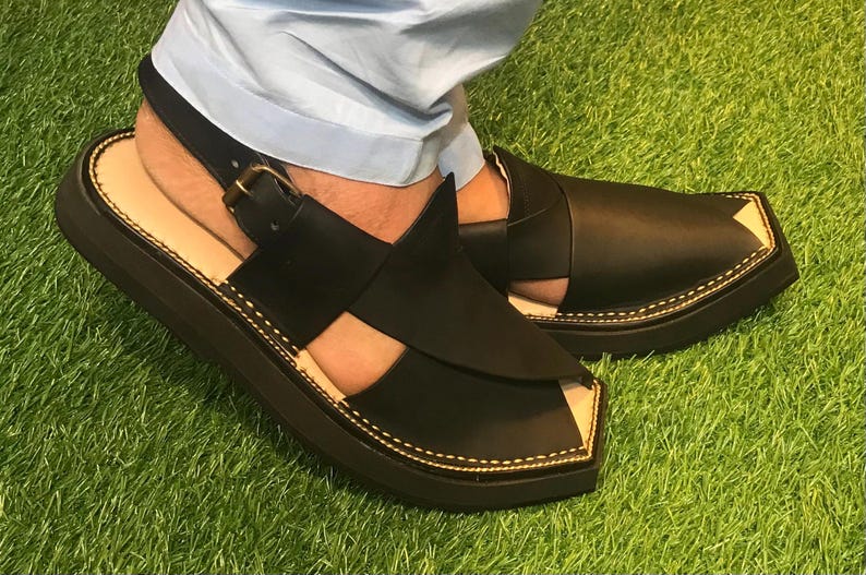May include: Black leather sandals with a closed toe and an open heel. The sandals have a thick sole and a strap that goes around the ankle.