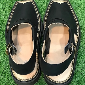 May include: A pair of black leather sandals with a gold buckle and a stitched design around the edge. The sandals have a flat sole and are made of a soft, supple leather.
