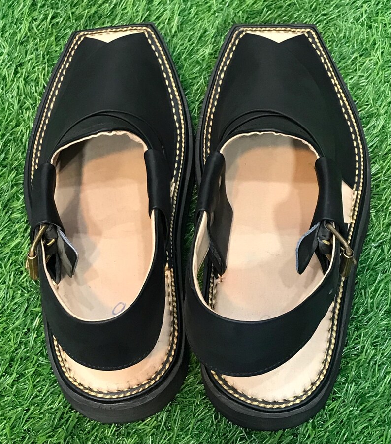 May include: A pair of black leather sandals with a gold buckle and a stitched design around the edge. The sandals have a flat sole and are made of a soft, supple leather.