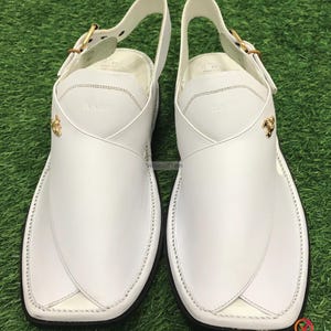 May include: A pair of white leather sandals with a buckle strap and gold accents. The sandals have a pointed toe and a flat sole.