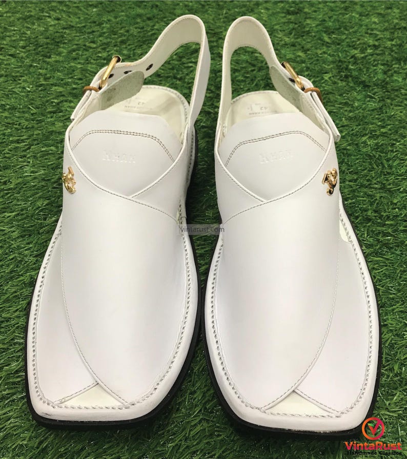 May include: A pair of white leather sandals with a buckle strap and gold accents. The sandals have a pointed toe and a flat sole.