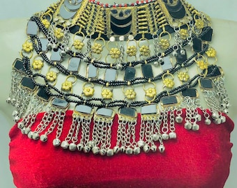 May include: An ornate necklace with a red velvet base. The necklace features layers of black, silver, and gold-toned metalwork, including floral accents, square mirrored elements, and dangling chains with small bells. The design is intricate and detailed.