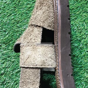 May include: A pair of brown suede sandals with a thick brown sole. The sandals have a strap across the top of the foot and an open toe.