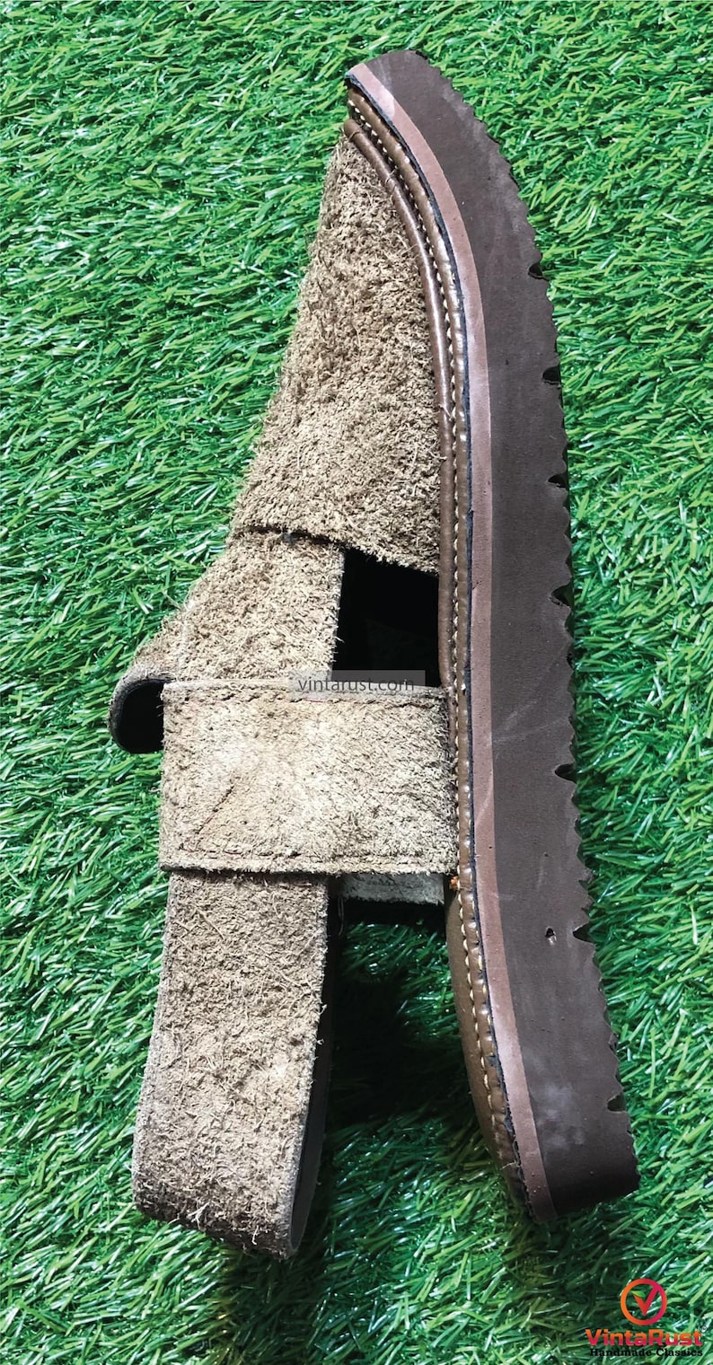 May include: A pair of brown suede sandals with a thick brown sole. The sandals have a strap across the top of the foot and an open toe.