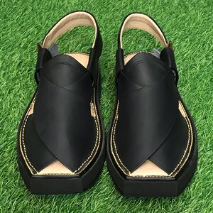 May include: A pair of black leather sandals with a closed toe and a strap across the top of the foot. The sandals have a gold stitching detail around the edges.