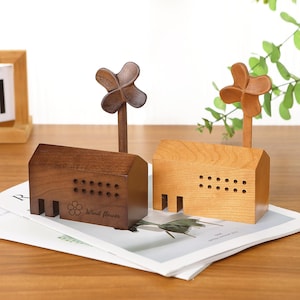 May include: Two wooden house-shaped music boxes. One is dark brown, the other is light brown. Each has a windmill on top and a flower and the words "Wind flower" on the front. The houses have small rectangular cutouts.