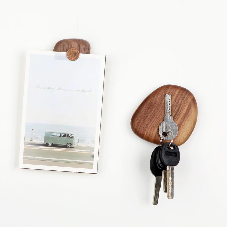 May include: Wooden key holder with a natural, pebble-like shape. A set of keys hangs from the holder. A small wooden clip holds a photo with a vintage van image. The photo has the text "Your attitude determines your height."