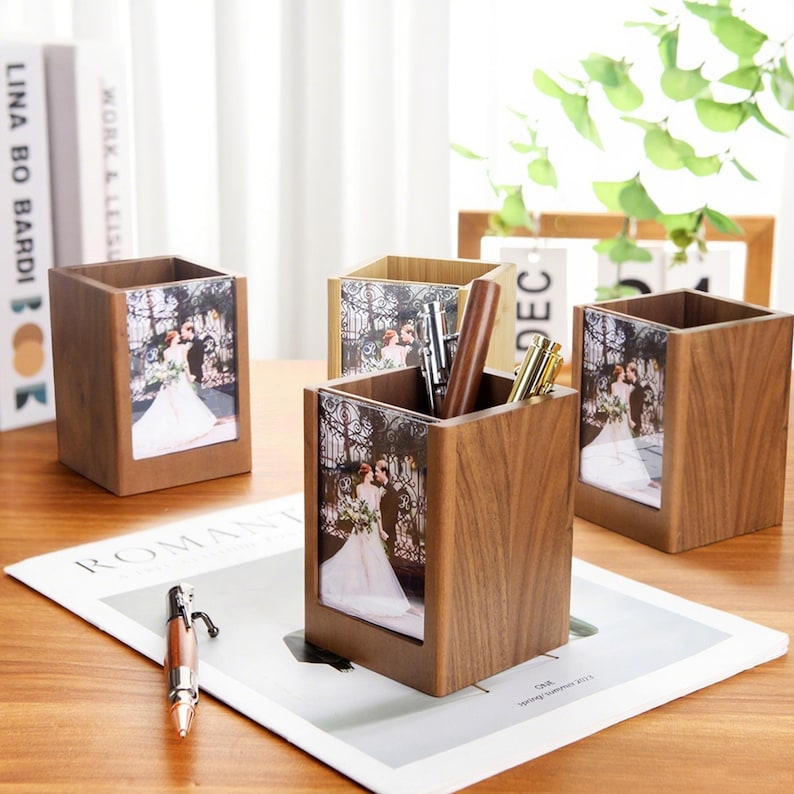 May include: Wooden pen holders with a photo frame design. The holders are square and feature a wedding photo. Pens are visible inside one of the holders. The holders are on a wooden surface with a magazine and books in the background.