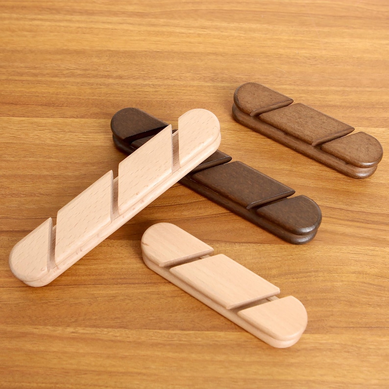 May include: Four wooden bread slicers in various shades of brown and natural wood. Each slicer has a unique design with a series of angled slots for guiding a knife. The items are arranged on a wooden surface.