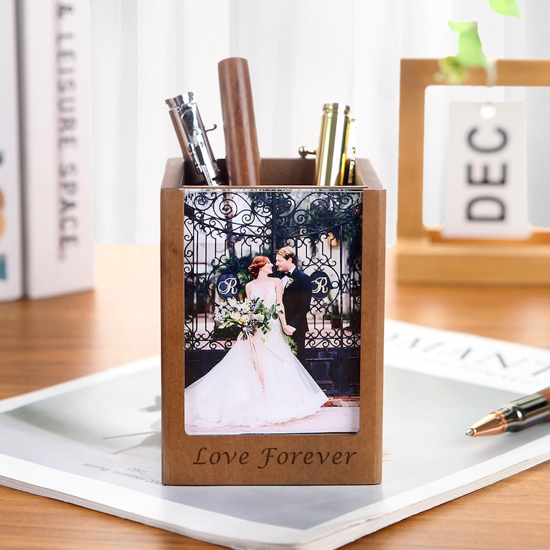 May include: A wooden pen holder with a photo of a couple in front of a wrought iron gate. The pen holder has the words "Love Forever" engraved on the front. Several pens are inside the holder.
