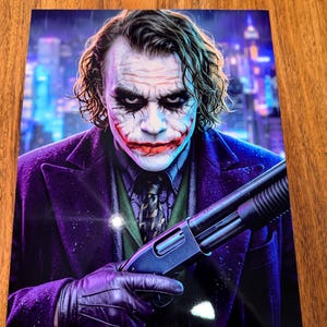 May include: A rectangular print featuring a portrait of the Joker with messy green hair, white face paint, and a red smile. The character wears a purple coat, green vest, and patterned tie, holding a black pump-action shotgun in a gloved hand.