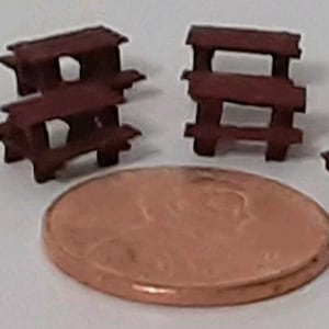 May include: Four miniature wooden picnic tables in a dark brown color. The tables are made of wood and have a simple design. They are all the same size and are arranged in a row.