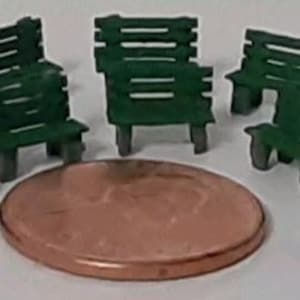 May include: A set of ten miniature green park benches made of plastic. The benches are arranged in a circle on a brown surface.