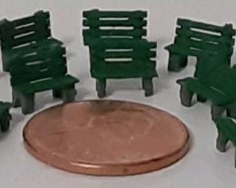 May include: A set of ten miniature green park benches made of plastic. The benches are arranged in a circle on a brown surface.