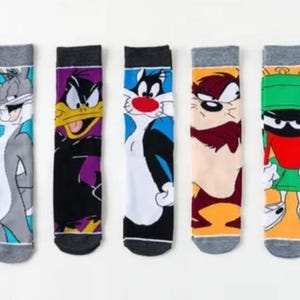 May include: Five pairs of colorful socks featuring cartoon characters from Looney Tunes. The socks are white with a grey, black, blue, orange, or green cartoon character on each sock.