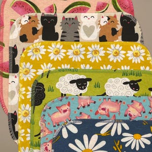 May include: A stack of colorful, patterned fabric squares. Designs include watermelons, cats, daisies, sheep, and pigs. Each square has a contrasting edge stitch.