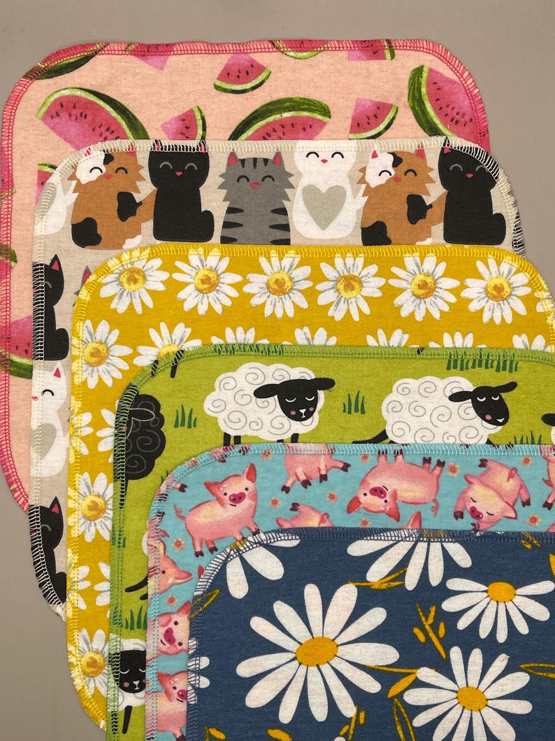May include: A stack of colorful, patterned fabric squares. Designs include watermelons, cats, daisies, sheep, and pigs. Each square has a contrasting edge stitch.