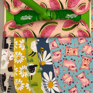 May include: A green Swiffer mop with a pink watermelon-patterned pad. Below are several patterned cleaning pads: cats, daisies, sheep, more daisies, and pigs. The pads are made of fabric and have rounded edges.