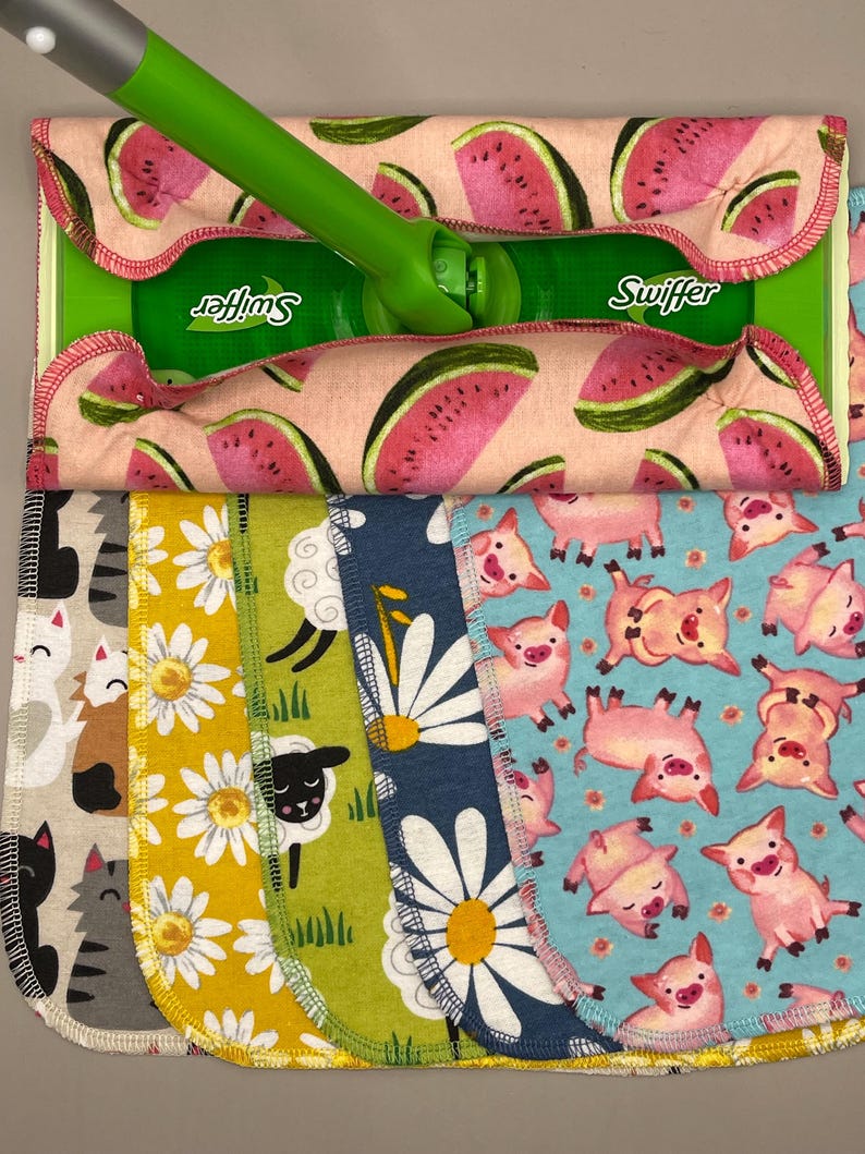 May include: A green Swiffer mop with a pink watermelon-patterned pad. Below are several patterned cleaning pads: cats, daisies, sheep, more daisies, and pigs. The pads are made of fabric and have rounded edges.