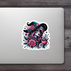 Pode incluir: Um adesivo com uma bruxa de cabelo rosa e azul, usando um chapéu preto adornado com flores. Ela segura uma xícara rosa, cercada por elementos florais. O design tem uma estética do Dia dos Mortos.